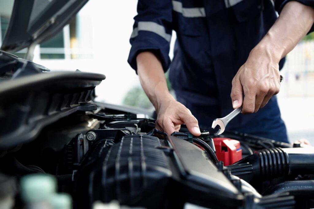 Technician using a wrench beneath an open vehicle hood.